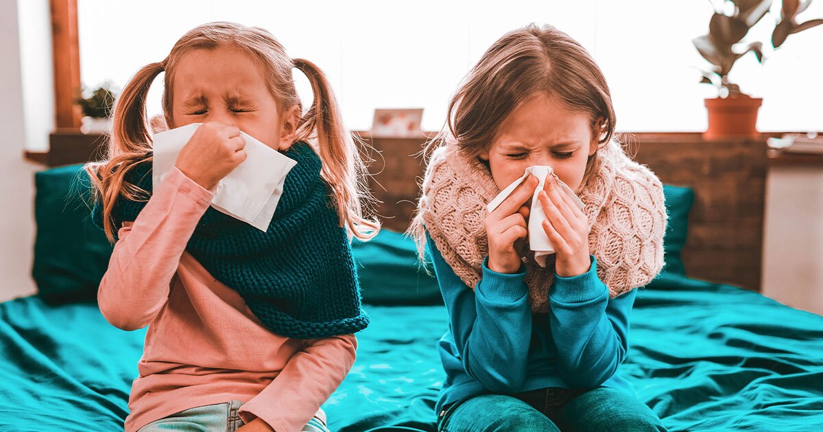 two little girls blowing their nose inside in their pajamas